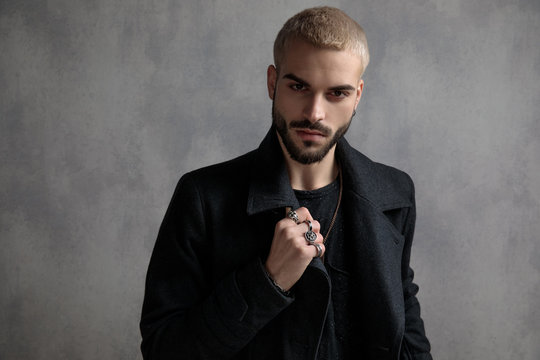 Confident young man adjusting his coat and showing his rings