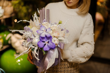 Girl holding a christmas composition with purple and white orchids and roses, tapes and candles in the box