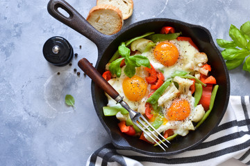 Fried eggs with vegetables in a pan on a gray concrete background. View from above.
