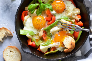 Fried eggs with vegetables in a pan on a gray concrete background. View from above.