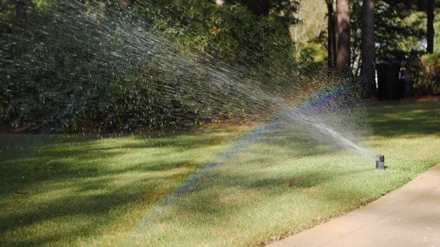 Rainbow created by irrigation lawn sprinkler heads watering grass. Automatic watering system spraying water in residential yard.