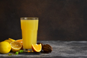 Orange juice, oranges and and juicer on stone background. Horizontal shot.