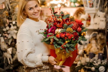 Smiling woman holding a red box with gold tape with different bright flowers decorated with fir-tree branches