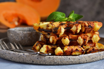 Belgian waffles with pumpkin and chocolate sauce on a concrete background with place for text.