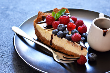 Homemade vanilla cheesecake with chocolate sauce and berries on a concrete background.