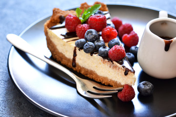 Homemade vanilla cheesecake with chocolate sauce and berries on a concrete background.