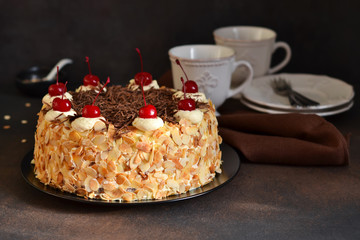 Chocolate cake with vanilla cream, cherry and almonds on a dark background.