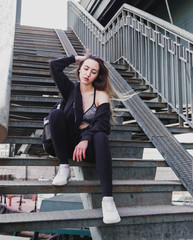 white beautiful young woman in black  sitting on a ladder on the street