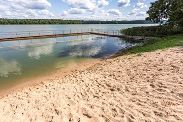 pier on sand shore of a large lake in summer day with beautiful clouds.  sky reflection