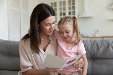 Happy mother embracing little daughter, reading greeting card
