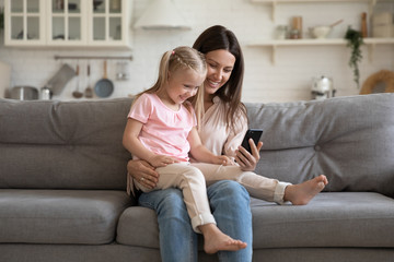 Happy young mother and little daughter having fun with phone