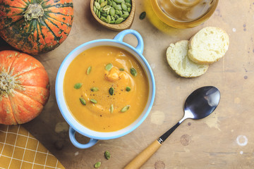 Pumpkin soup and organic pumpkins on rustic table.