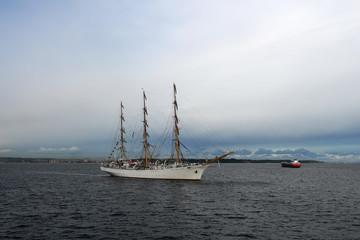 Fototapeta na wymiar Training sailing frigate goes to sea from the port against a stormy sky