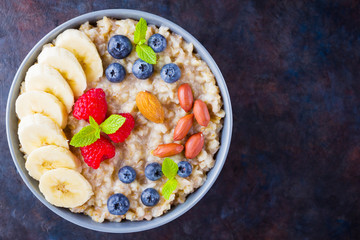 Healthy breakfast. Oatmeal with blueberries, banana and raspberry. Oatmeal with fruits and nuts in a bowl. Cooked oatmeal on dark background. Vegetarian food