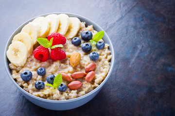 Healthy breakfast. Oatmeal with blueberries, banana and raspberry. Oatmeal with fruits and nuts in a bowl. Cooked oatmeal on dark background. Vegetarian food