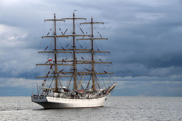 Fototapeta na wymiar Training sailing frigate goes to sea from the port against a stormy sky