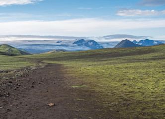 Icelandic landscape with footpath of Laugavegur hiking trail with view on Tindfjallajokull glacier, green hills and lava gravel ground covered by grass and moss. Fjallabak Nature Reserve, Iceland