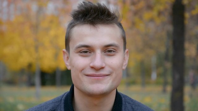 Young handsome man posing for camera in autumn park, happy and healthy life concept