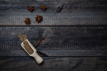 Fototapeta premium Anise stars and scoop of anise on a dark wooden table. The concept of using spices for dishes, enriching the taste.