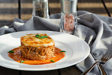 Close-up of a traditional lasagna made with minced beef bolognese sauce topped with basil leafs served on a white plate