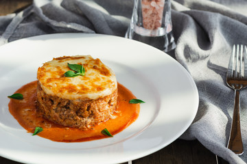 Close-up of a traditional lasagna made with minced beef bolognese sauce topped with basil leafs served on a white plate