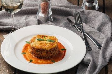 Close-up of a traditional lasagna made with minced beef bolognese sauce topped with basil leafs served on a white plate