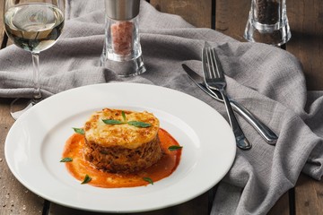 Close-up of a traditional lasagna made with minced beef bolognese sauce topped with basil leafs served on a white plate