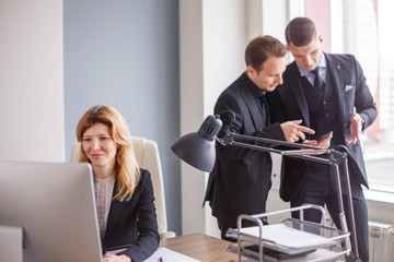 Woman working on pc and men discussing in the background in modern office.