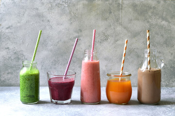 Assortment of colorful smoothies in a bottles with paper straws.