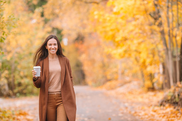 Fall concept - beautiful woman drinking coffee in autumn park under fall foliage