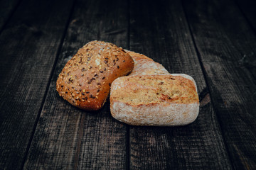 Fresh rolls on a dark wooden background. The concept of baking bread, eating meals with rolls, bread. Product made of wheat and rye flour, bread preparation. Eating sandwiches.