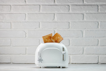 Roasted toast bread popping up of toaster with white brickwall
