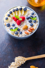 Healthy breakfast with milk. Oatmeal with fruits, nuts and honey. Oatmeal with blueberries, banana and raspberry. Cooked oatmeal on dark background