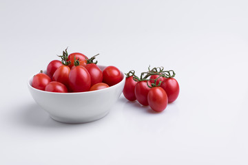 Grape or cherry tomato branch. Pile of red grape tomatoes isolated on white background, soft light