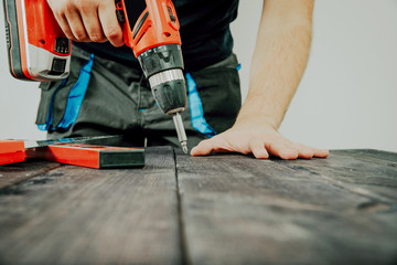 The worker uses a screwdriver to work in wood, boards. The concept of working with wood, boards. Building a table, wooden tops. Caring for details at work.