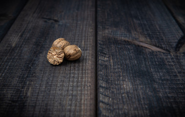 The whole nutmeg on a dark wooden table top. The concept of eating and adding spices to dishes. Improving the taste of dishes, sharp expressive taste.