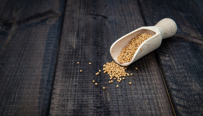 Mustard with a scoop on a dark wooden countertop. The concept of eating and adding spices to dishes. Improving the taste of dishes, sharp expressive taste.
