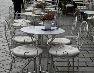 Dainty White Curving Cafe Table Row with Seat Cushions and Heather Pots Outdoors in Bratislava Slavakia
