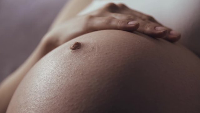 Close-up of pregnant woman with baby moving and kicking inside belly, she carefully touch tummy and playing with her baby. Last trimester of pregnancy