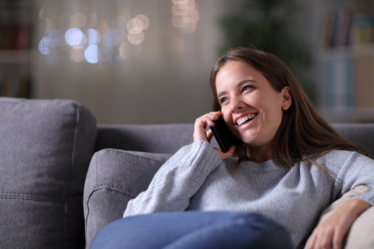 Happy woman talking on phone on a couch in the night