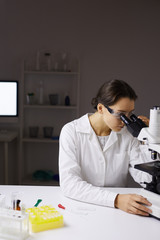 Portrait of young female scientist looking in microscope while doing research in medical laboratory, copy space