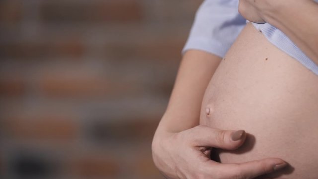 Close-up pregnant belly, future mother indoors in living appartment carefully touch tummy and playing with her baby. Second trimester of pregnancy