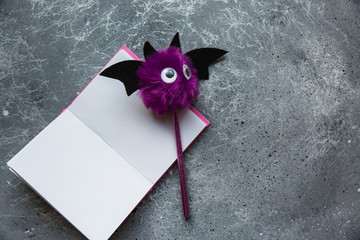 Trendy purple bat pencil and pink notebook for notes on grey background. Halloween still life. Flat lay