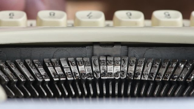 Close up of the strikers on a 1950's era manual typewriter from Germany.  Out of focus hands typing in the background.