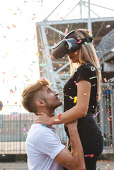 Fototapeta na wymiar beautiful couple in love having fun in a rain of colorful confetti with virtual reality glasses