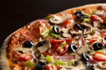 Close-up of fresh homemade Pizza seen from above, on dark wooden table.