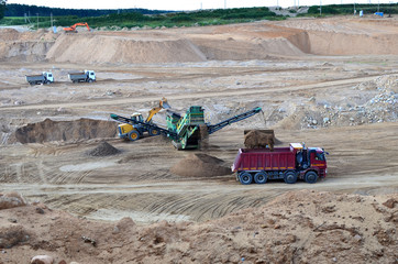 Wheel front-end loader loads sand into a dump truck. Heavy machinery in the mining quarry, excavators and trucks. Mobile jaw crusher plant with belt conveyor puts crushing and screening process