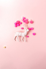 White reindeer toy with small balls of wool on pink pastel background.