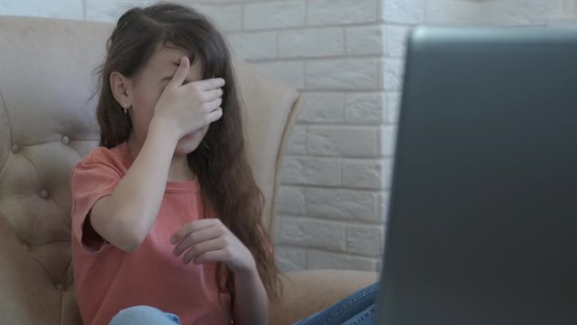 Video not for child. A little girl watches a movie on a laptop and covers her eyes with her hand.