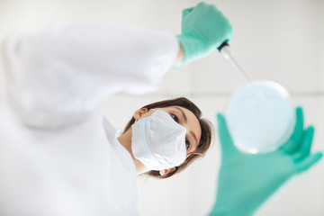 Directly below view of young woman holding petri dish with test samples during medical research in...